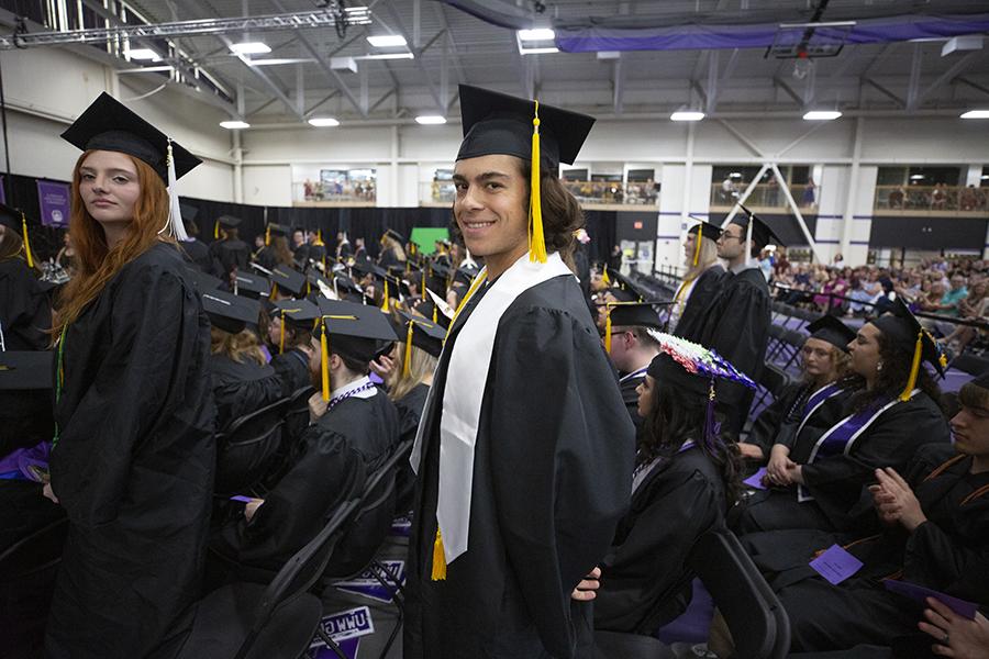 A student wearing their cap and gown smiles at the camera during graduation.