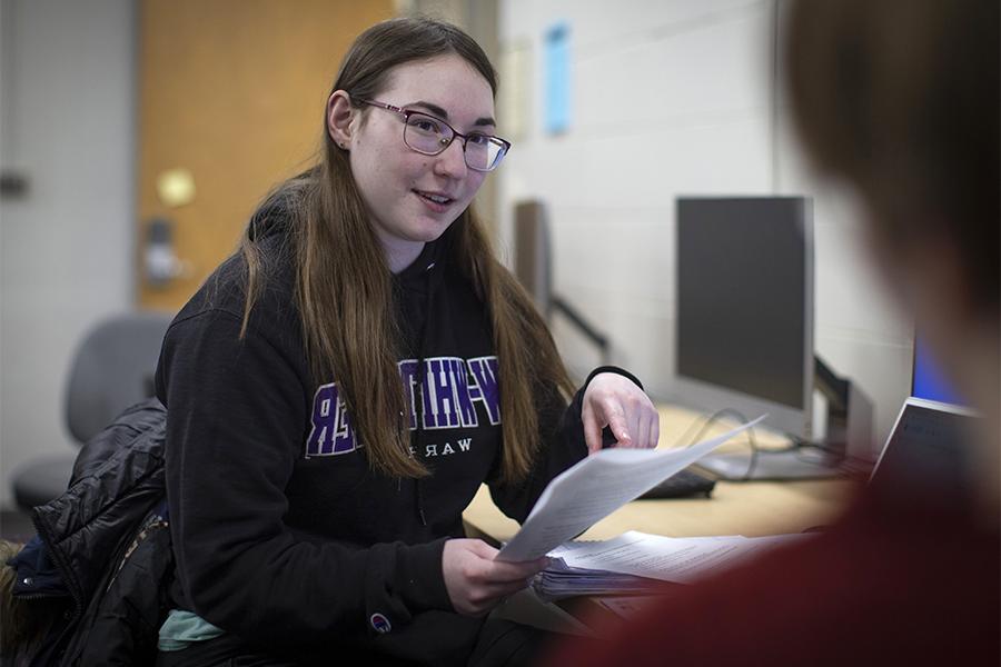 A student holds a book while working on a laptop.