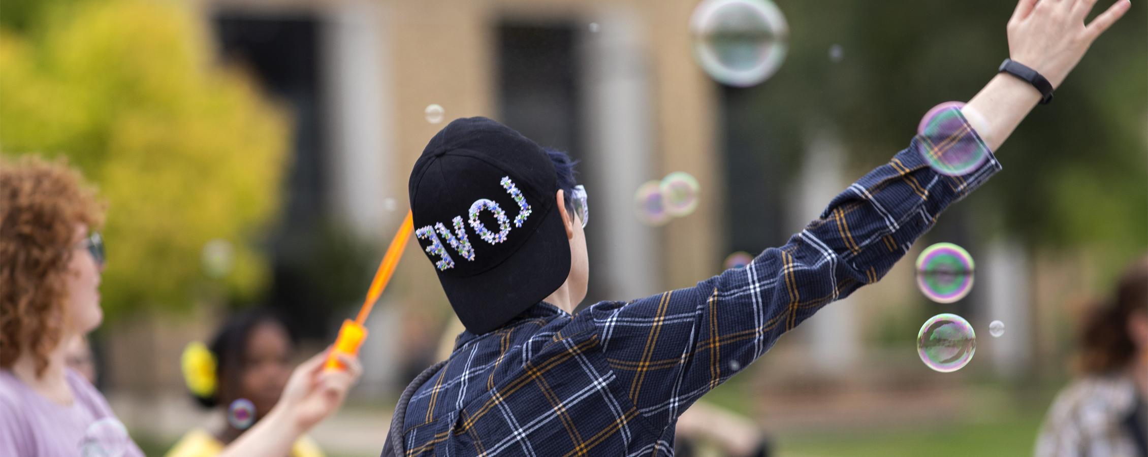 A person wears a hat that says love while bubbles float in the air.