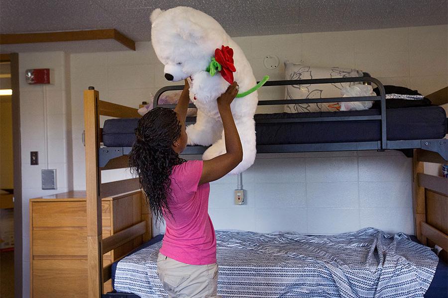 Student lifts large teddy bear in dorm room.