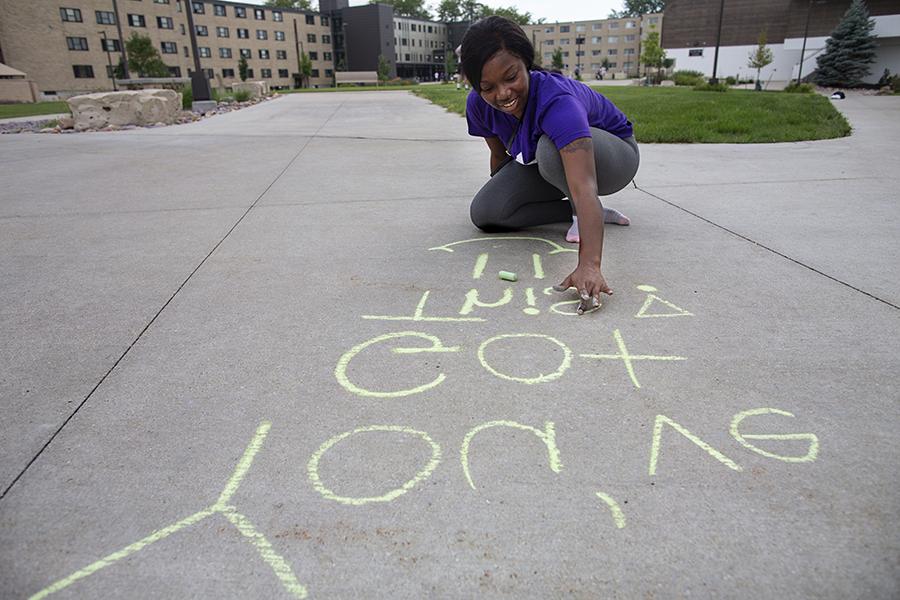 A student writes positive messages with chalk on a sidewalk.