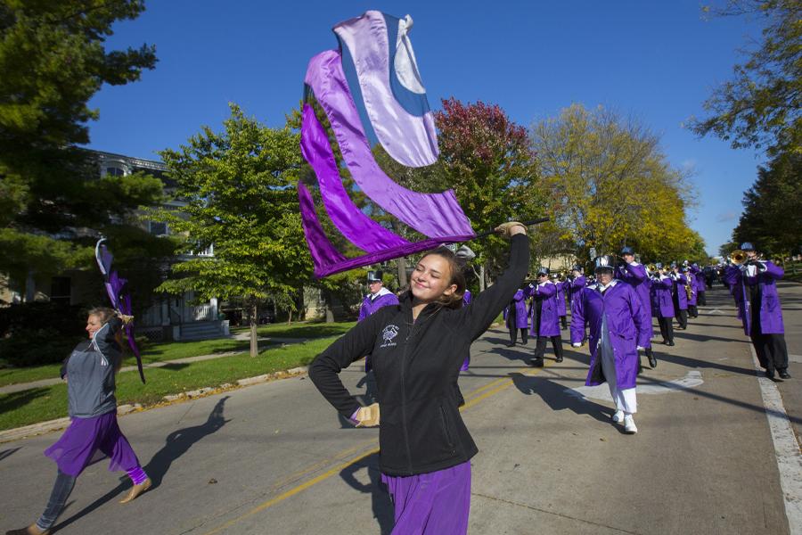 A person wearing purple waves a purple flag in a parade that marches down the street.