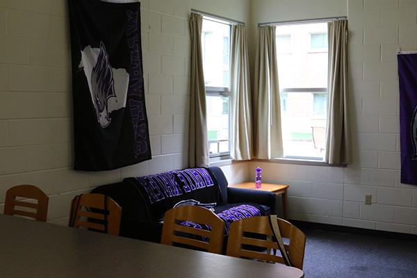 A living room with 2 windows, a couch, and a side table inside of it.