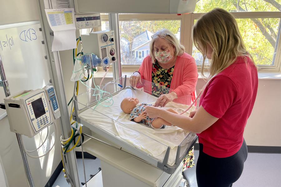 A student works with a faculty member in a simulated nursery with a baby doll.