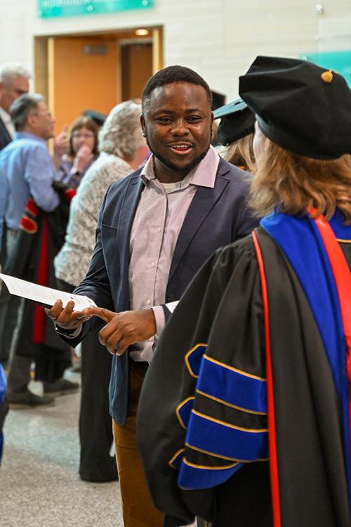 Patrice Achu speaks with a person wearing graduation Regalia.