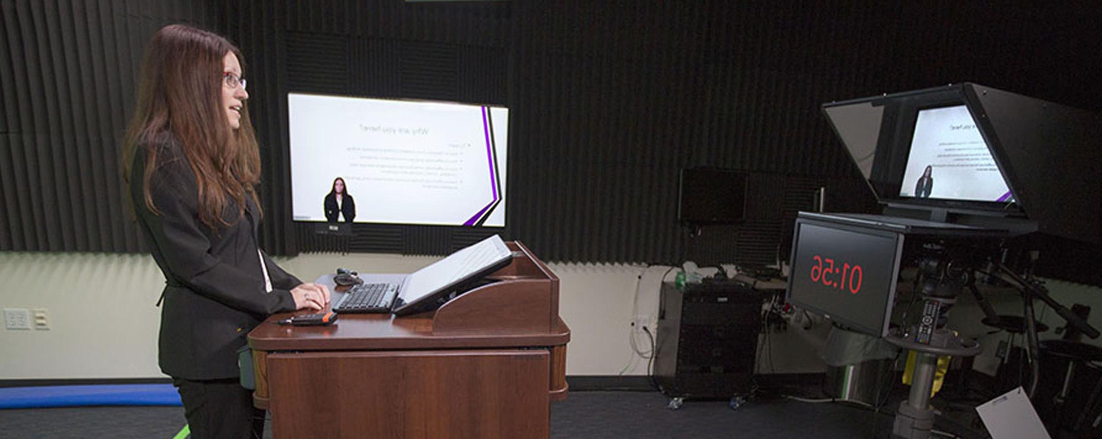 A faculty member speaks at a podium while being recorded.