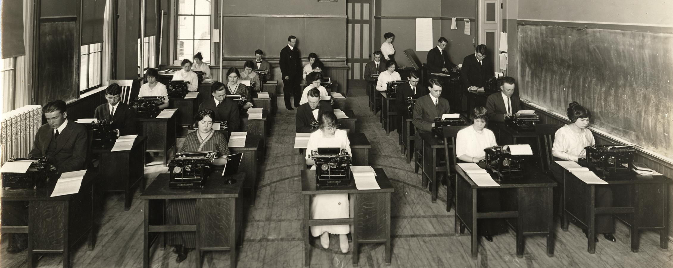 An old photo shows business students sitting at desks with typewriters in the earliest days of the business school.