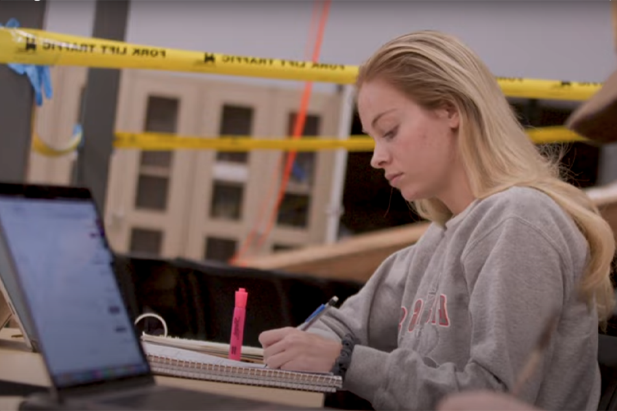 A student writes in a notebook while sitting in class with caution tape behind her.