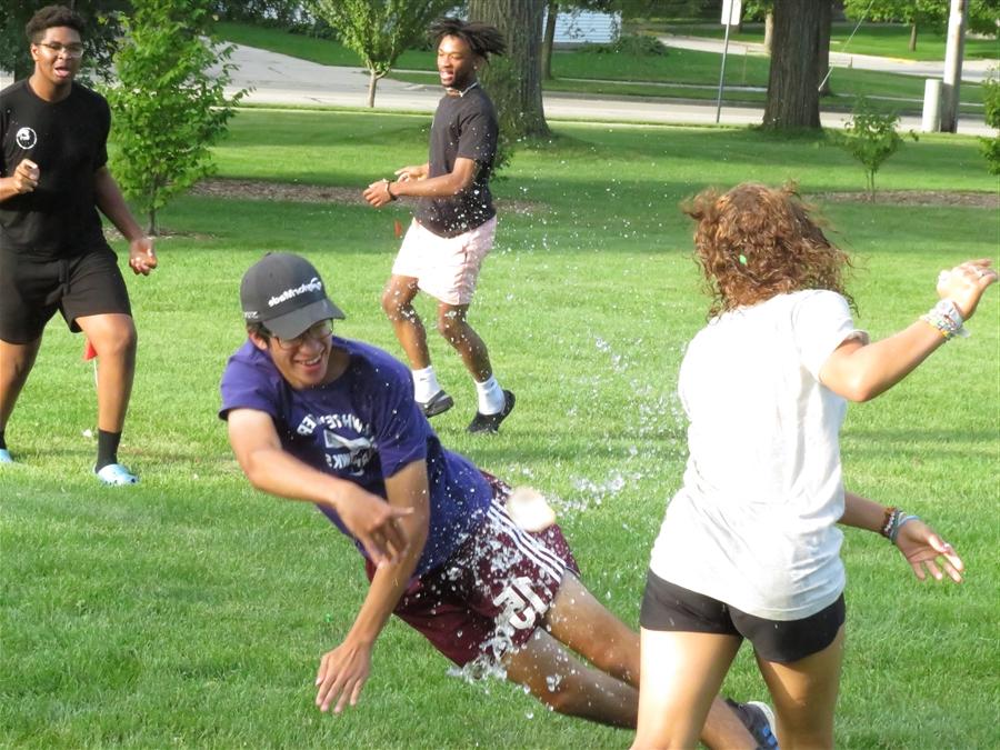 Students playfully throw water at each other outdoors.